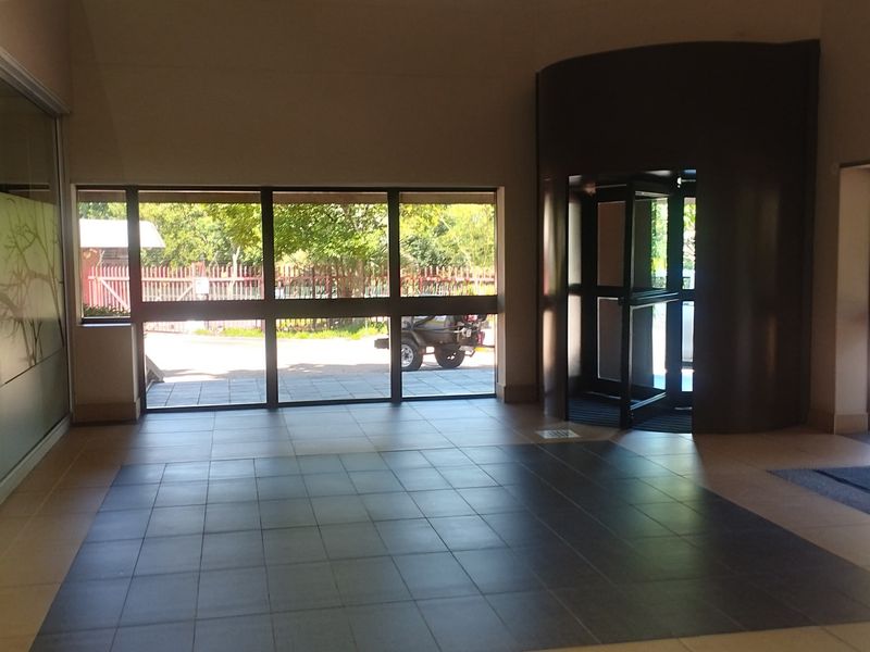 Spacious commercial entrance lobby featuring tiled flooring, a modern revolving door, and large glass windows providing natural light and exterior views.