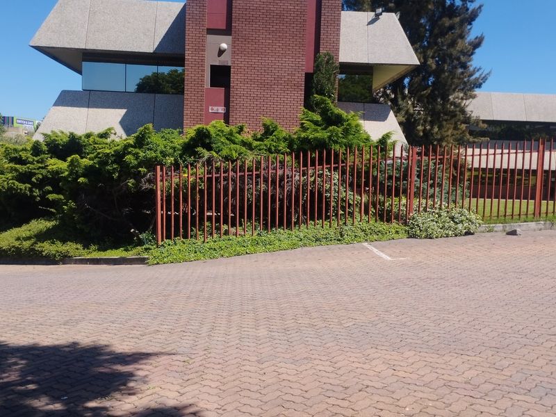 Front view of a commercial office building featuring a brick and concrete facade, reflective windows, and secure perimeter fencing with a paved driveway.