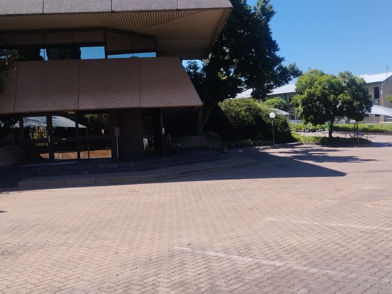 Exterior view of a commercial office building featuring a paved parking area, covered entrance, and mature landscaping.
