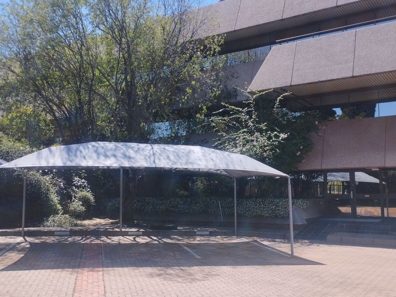 Exterior view of a multi-story commercial office building featuring a paved parking area with shade cloth carports and established garden landscaping.