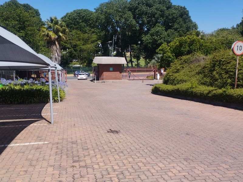 Commercial property entrance featuring a paved driveway, security guard house, gated access, and covered parking bays.