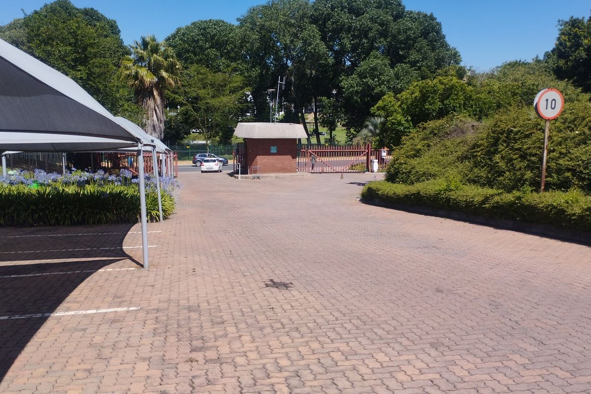 Commercial property entrance featuring a paved driveway, security guard house, gated access, and covered parking bays.