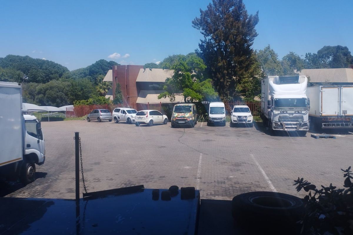 A paved commercial parking and loading yard area featuring perimeter fencing and views of the adjacent commercial building structure.