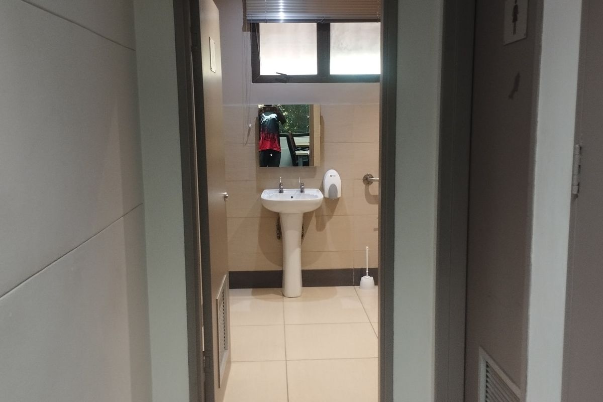 A clean, functional commercial bathroom featuring a pedestal basin, tiled walls and flooring, and a grab rail for accessibility.