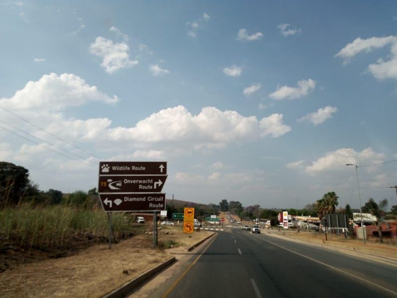 A view of a public road featuring directional signage for local routes and surrounding commercial infrastructure.