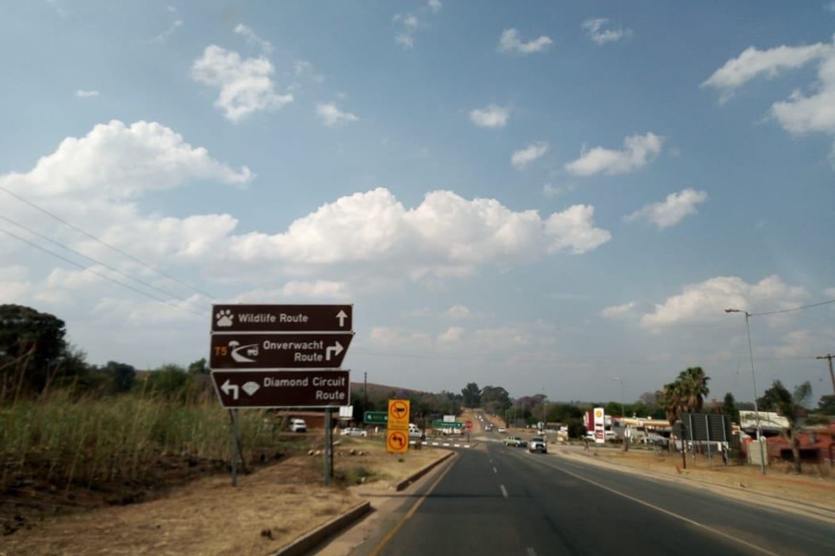 A view of a public road featuring directional signage for local routes and surrounding commercial infrastructure.