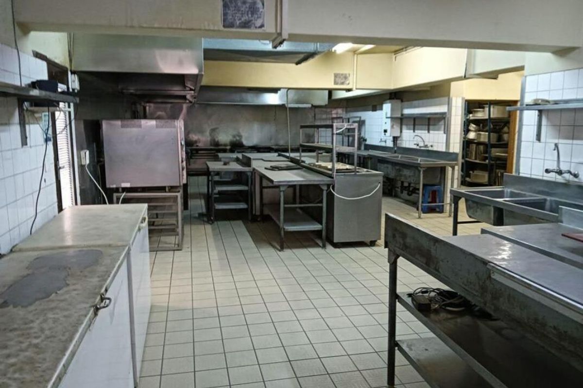 A functional commercial kitchen space featuring stainless steel work surfaces, industrial sinks, and an extractor hood, suitable for professional food preparation.