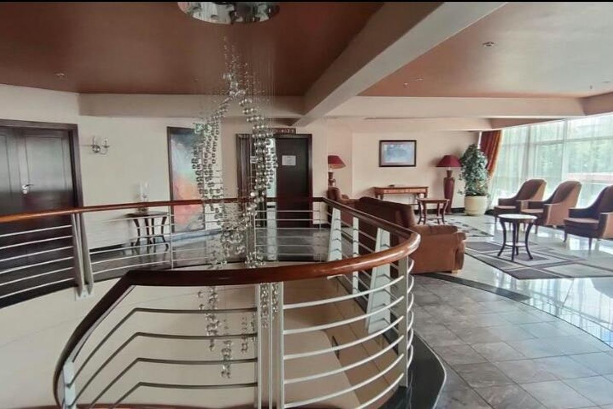 Spacious commercial lounge area featuring polished tile floors, a decorative central staircase with a stainless steel balustrade, and expansive windows providing natural light.