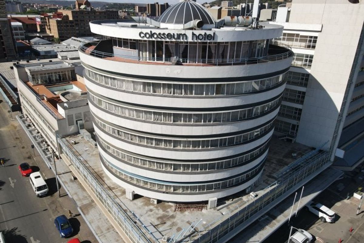 Aerial view of the circular Colosseum Hotel building, showcasing its multi-story facade, rooftop dome structure, and surrounding urban street environment.