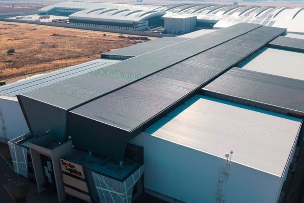 Aerial view of a large-scale industrial logistics facility featuring extensive metal roofing, integrated solar panels, and secure perimeter fencing.