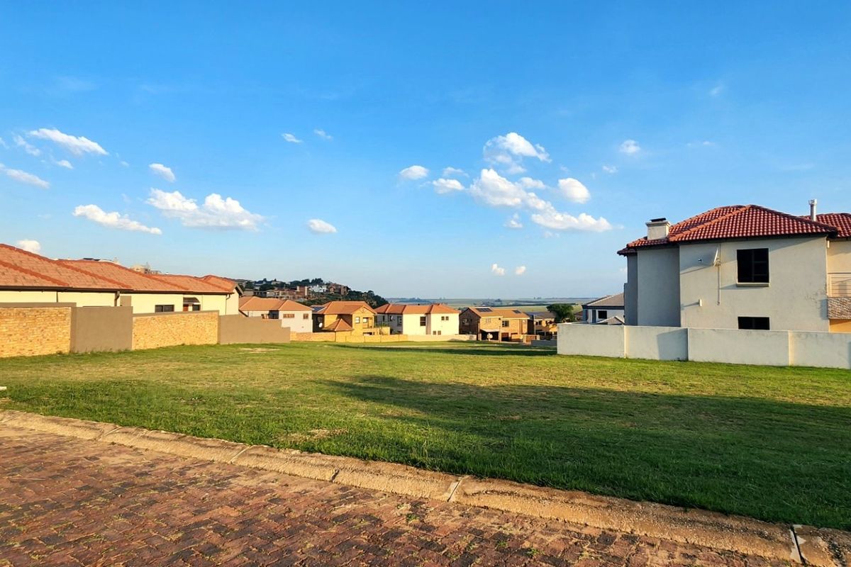 A vacant residential plot featuring a grass lawn, paved street frontage, and established boundary walls in a developed neighborhood setting.