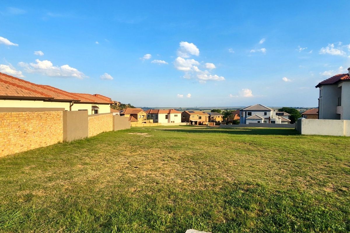 A vacant residential plot featuring a grass lawn and boundary walls, situated within a developed neighborhood with surrounding houses.