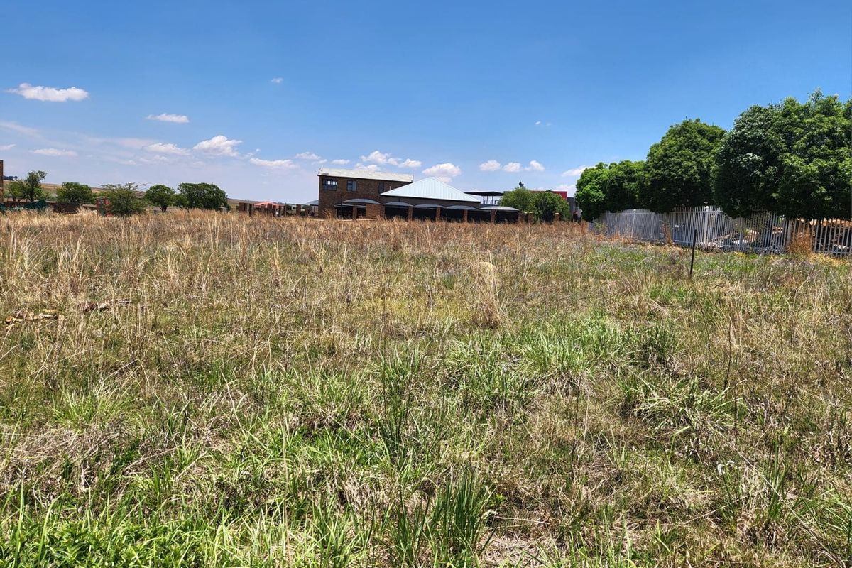 A vacant residential plot featuring natural grass cover and perimeter fencing, offering a clear view of the surrounding neighborhood.