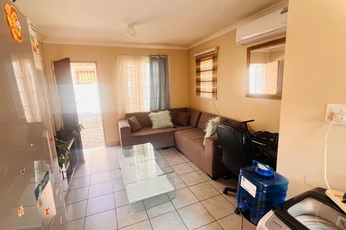 A compact living area featuring tiled flooring, a wall-mounted split-system air conditioner, and natural light through window blinds.