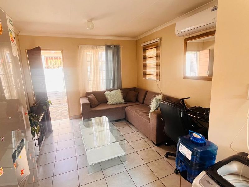 A compact living area featuring tiled flooring, a wall-mounted split-system air conditioner, and natural light through window blinds.