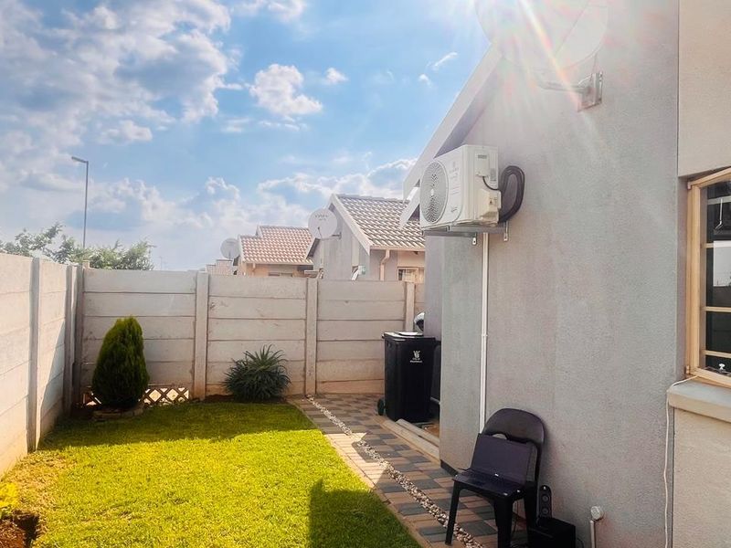 A private rear garden featuring a lawn, paved walkway, and precast concrete boundary wall, with an exterior air conditioning unit mounted to the house.
