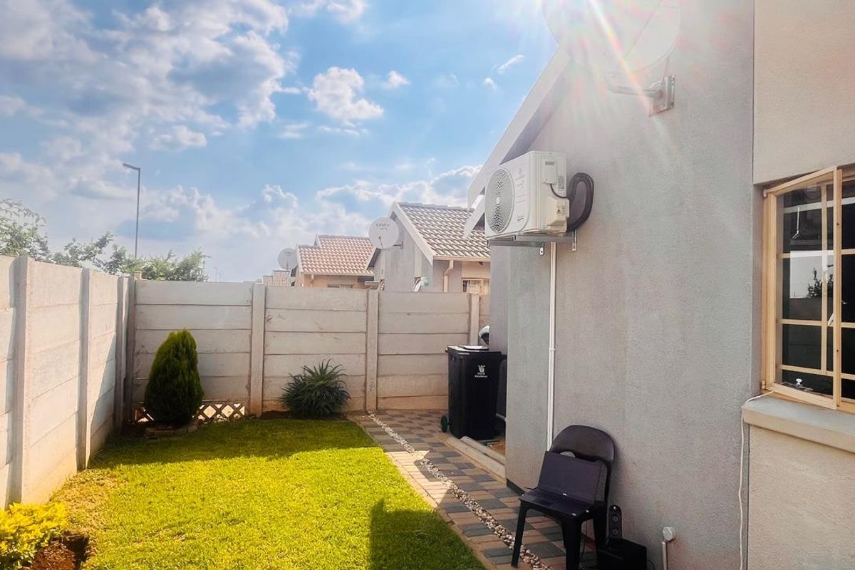 A private rear garden featuring a lawn, paved walkway, and precast concrete boundary wall, with an exterior air conditioning unit mounted to the house.