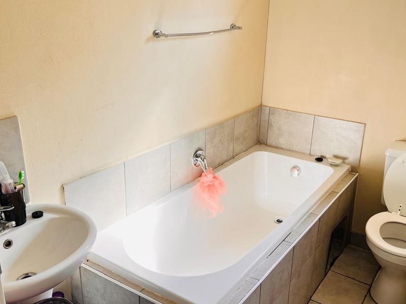 A functional bathroom featuring a built-in bathtub with wall-mounted faucet, pedestal sink, and standard toilet with tiled finishes.