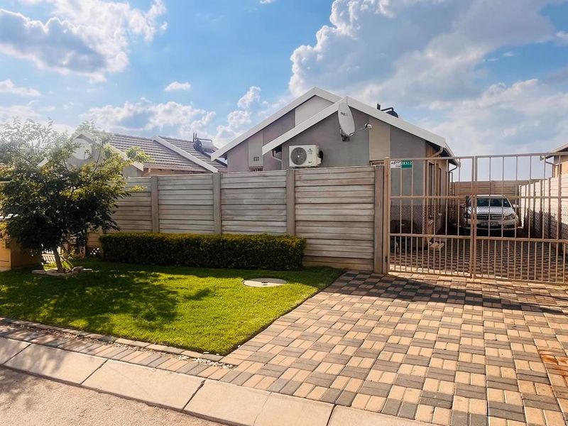 Front exterior view of the property featuring a paved driveway, secure metal gate, precast concrete boundary wall, and a well-maintained lawn area.
