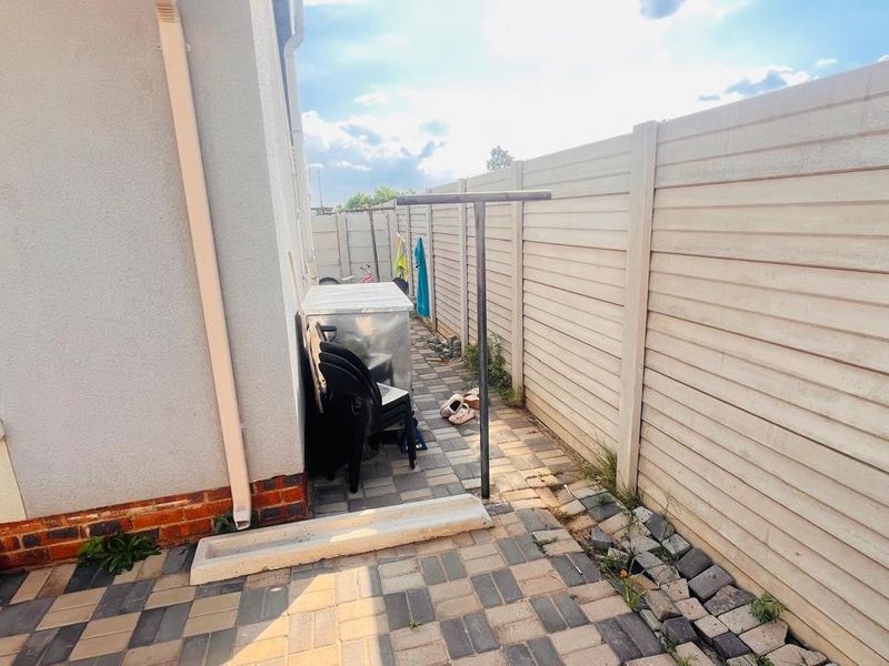 A narrow side passage featuring paved flooring, a precast concrete boundary wall, and a fixed washing line.