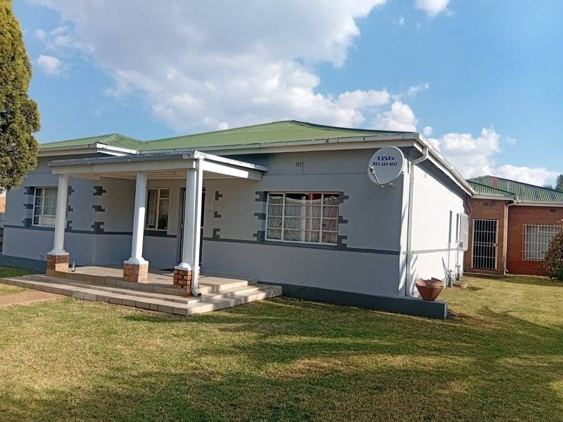 Front elevation of a single-story house featuring a covered porch, metal roofing, and security bars on windows, set within a lawned garden.