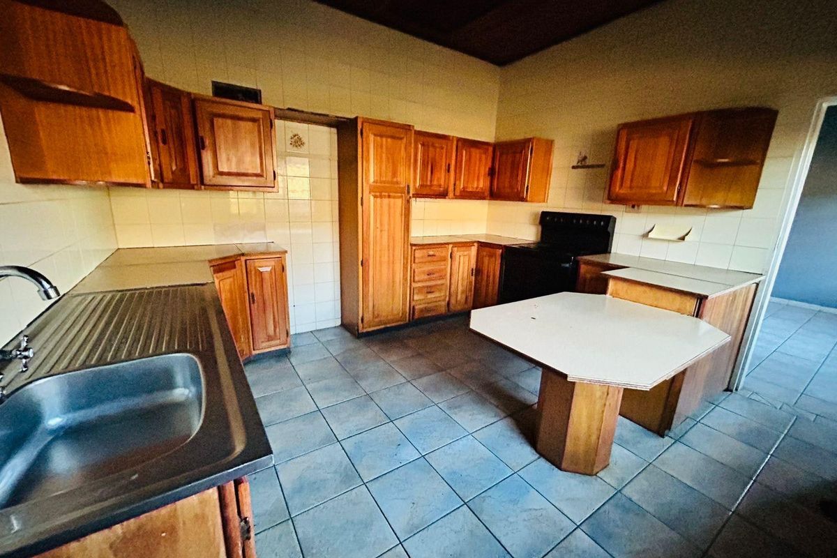 A dated kitchen featuring wooden cabinetry, tiled flooring, and a freestanding stove, offering a functional layout ready for modern renovation.