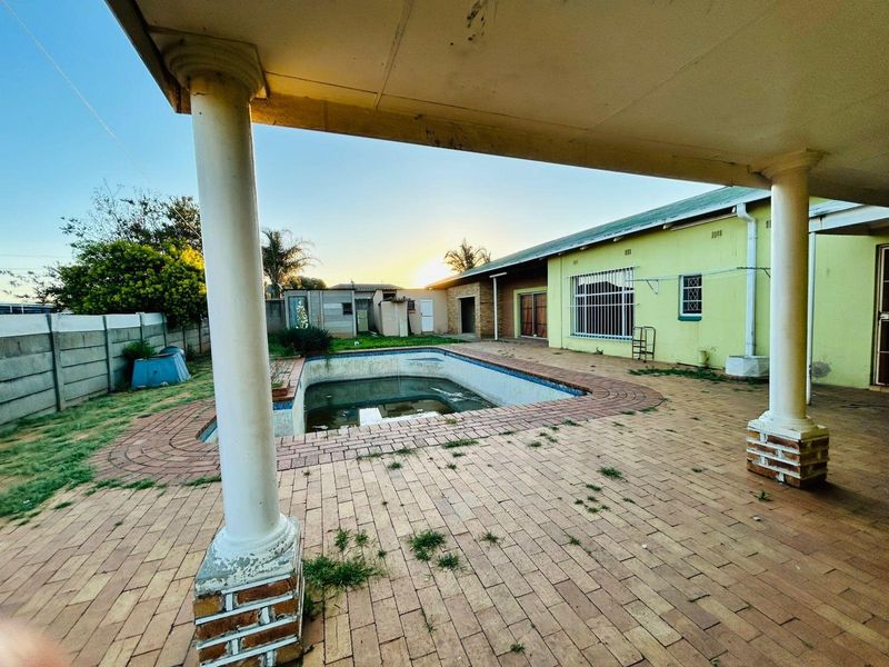 Outdoor pool area featuring a covered patio with concrete columns, brick paving, and a swimming pool requiring maintenance.