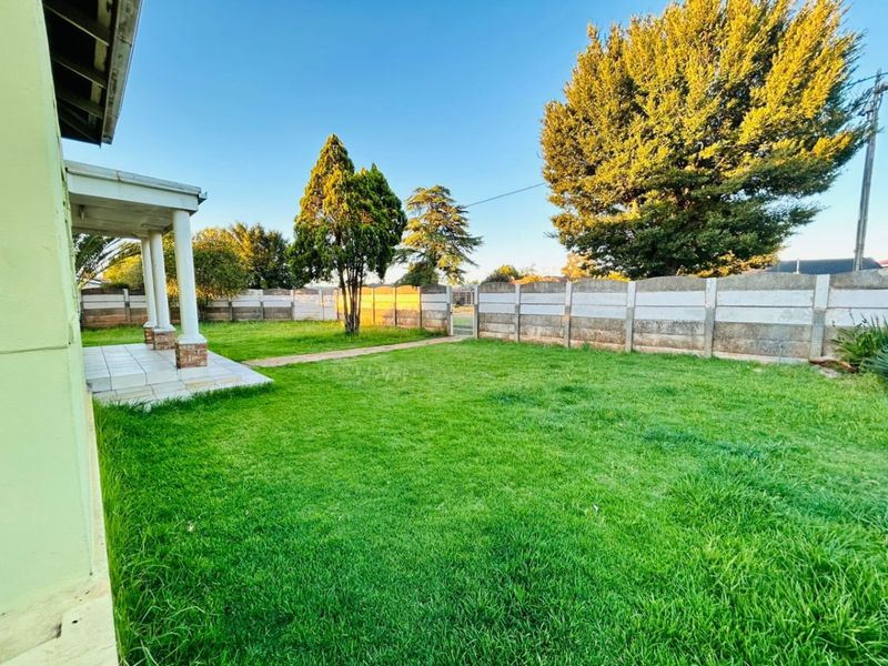 A spacious rear garden featuring a well-maintained lawn, a covered tiled patio with structural columns, and a secure precast concrete boundary wall.