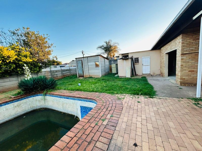 Rear garden area featuring a swimming pool, brick paving, and an outbuilding, requiring significant maintenance and landscaping to restore its appeal.