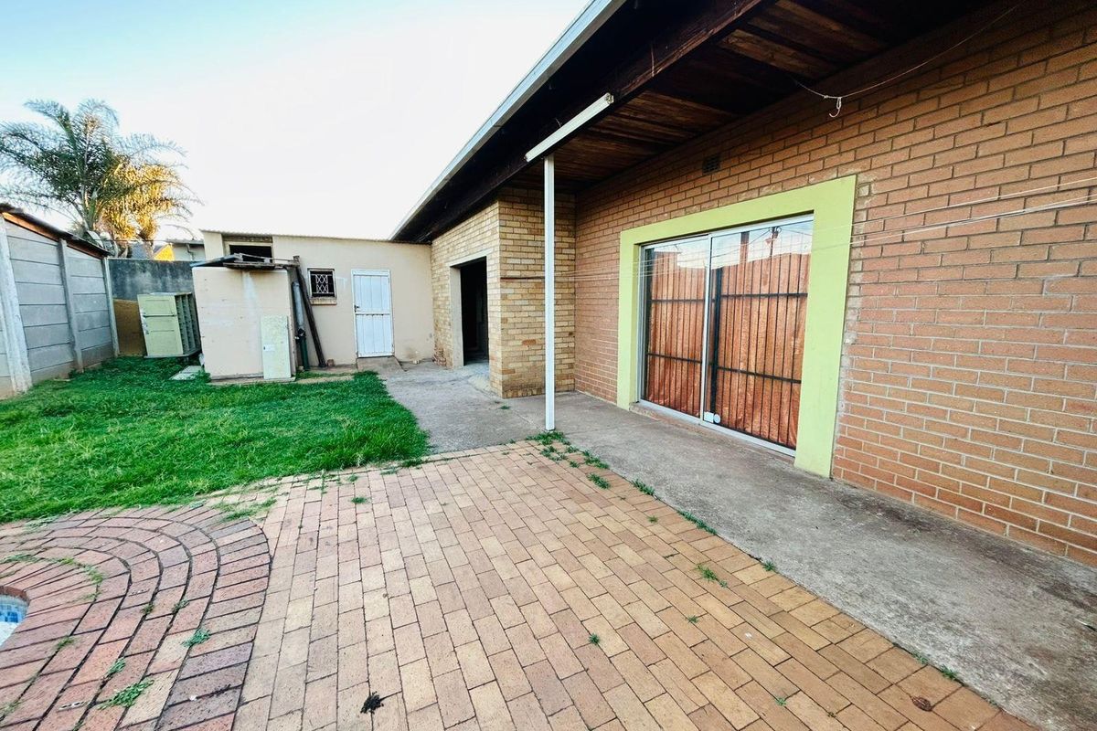 Rear exterior view featuring a brick facade, paved patio area, and sliding glass door access to the home.