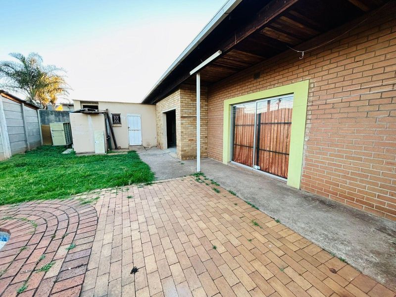 Rear exterior view featuring a brick facade, paved patio area, and sliding glass door access to the home.