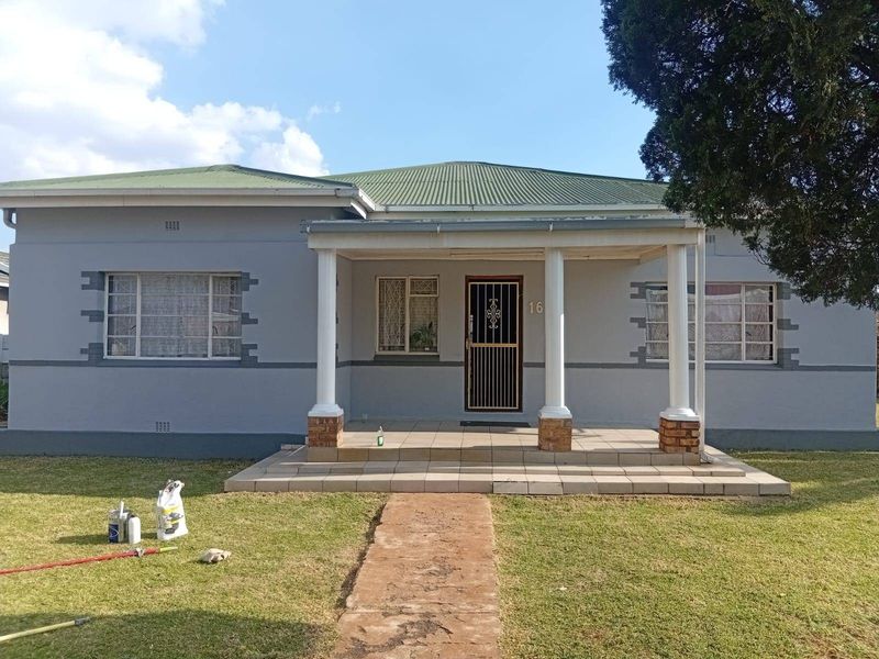Front elevation of a single-story house featuring a covered porch with concrete columns, a metal roof, and a secure entrance gate.