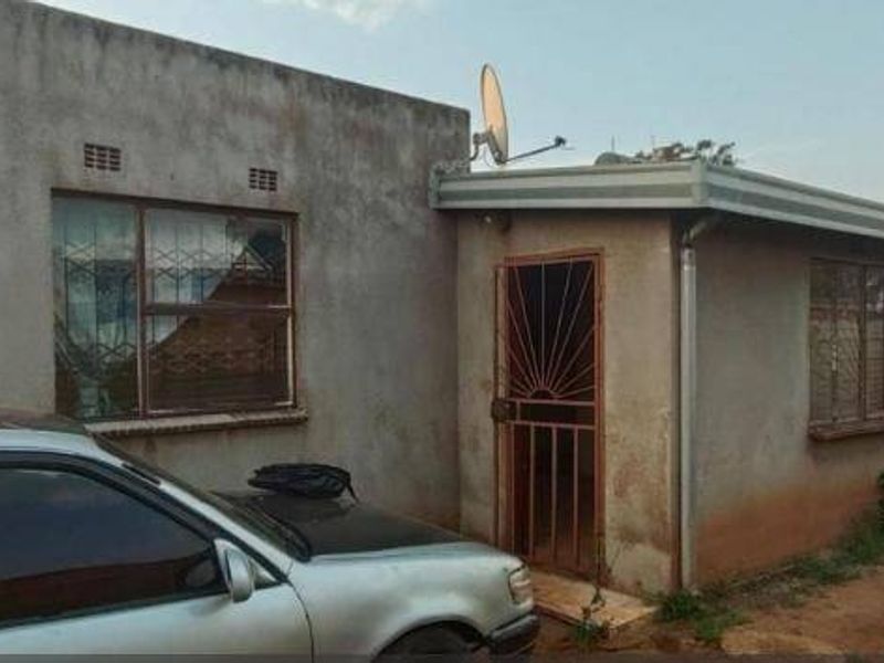 Rear exterior view of the property featuring a simple facade, security gate, and metal window frames with visible signs of weathering.