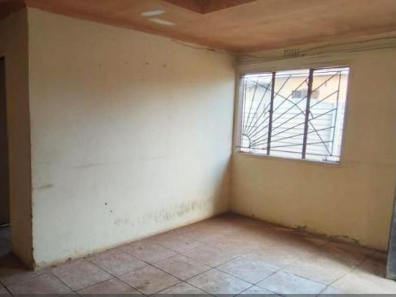 An empty living room featuring tiled flooring, a window with security bars, and a timber door, requiring cosmetic updates to the walls and ceiling.