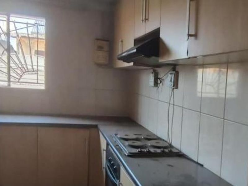 A compact kitchen featuring built-in cabinetry, an electric hob, oven, and extractor fan, requiring cosmetic updates to improve its overall condition and appeal.