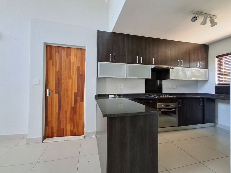 Modern kitchen featuring dark wood cabinetry, granite countertops, built-in oven, gas hob, and tiled flooring, presented in a clean, empty space.