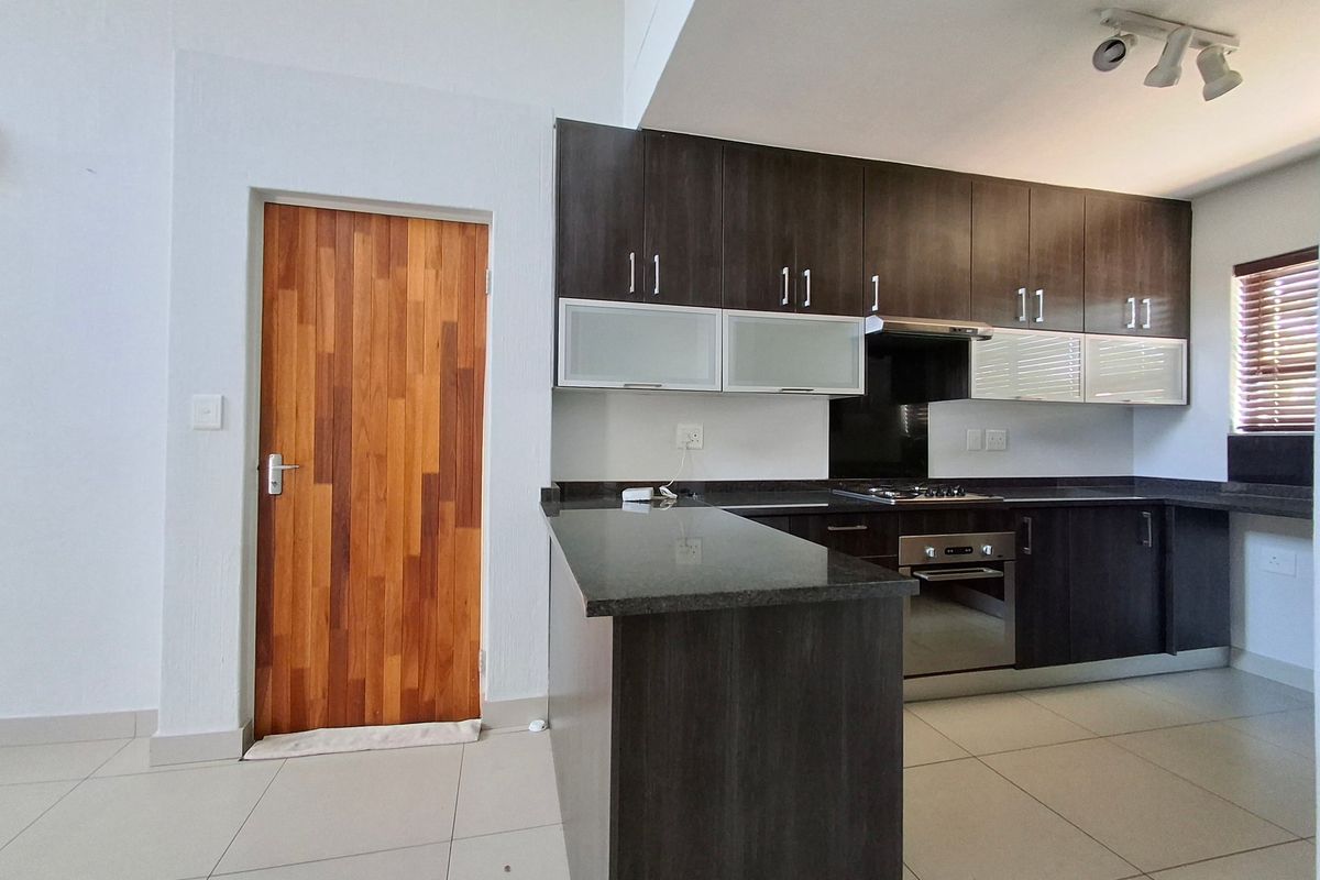 Modern kitchen featuring dark wood cabinetry, granite countertops, built-in oven, gas hob, and tiled flooring, presented in a clean, empty space.