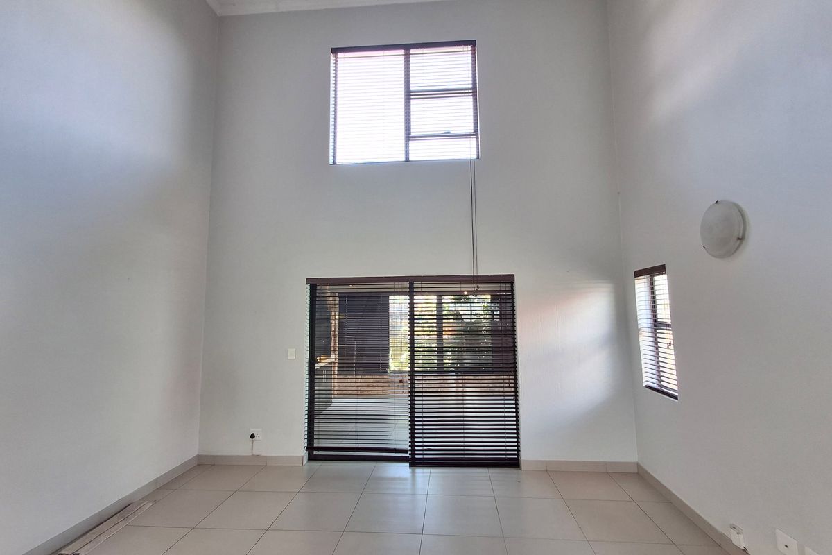 Spacious double-volume living area featuring tiled flooring, large sliding glass doors, and natural light, providing a versatile blank canvas for interior design.