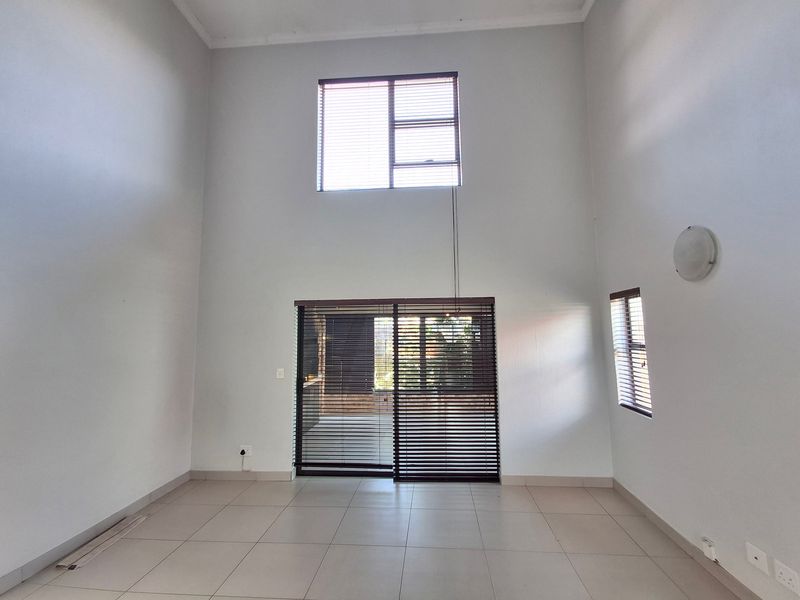 Spacious double-volume living area featuring tiled flooring, large sliding glass doors, and natural light, providing a versatile blank canvas for interior design.