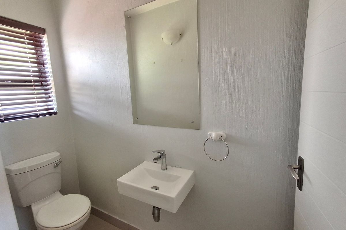 A clean and functional guest bathroom featuring a wall-mounted basin, chrome fixtures, and a simple mirror, finished with neutral wall tones.