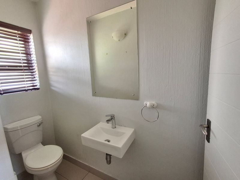 A clean and functional guest bathroom featuring a wall-mounted basin, chrome fixtures, and a simple mirror, finished with neutral wall tones.
