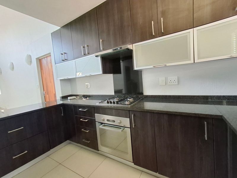 Modern kitchen featuring dark wood cabinetry, granite countertops, built-in oven, gas hob, and extractor fan with neutral tiled flooring.