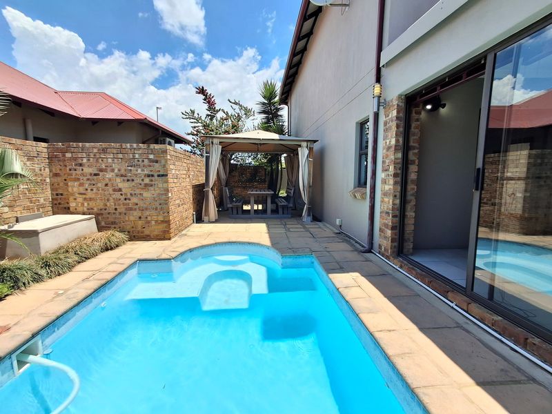A private outdoor pool area featuring a paved patio, brick boundary walls, and direct access to the home through large sliding glass doors.