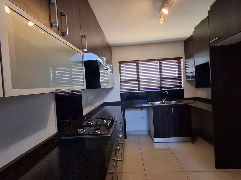 Modern kitchen featuring dark wood cabinetry, granite countertops, a gas hob with extractor fan, and tiled flooring.