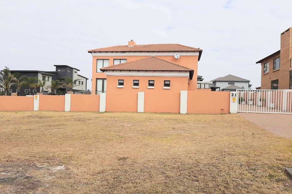 A view of a residential vacant plot featuring a boundary wall, gated entrance, and paved driveway, with a neighboring house in the background.