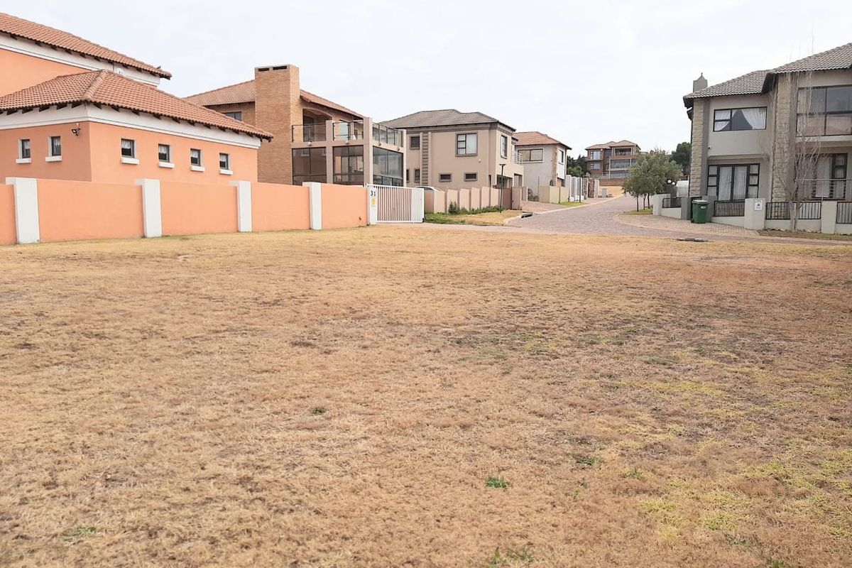 A vacant residential plot situated within a developed estate, featuring established boundary walls and access to a paved street.