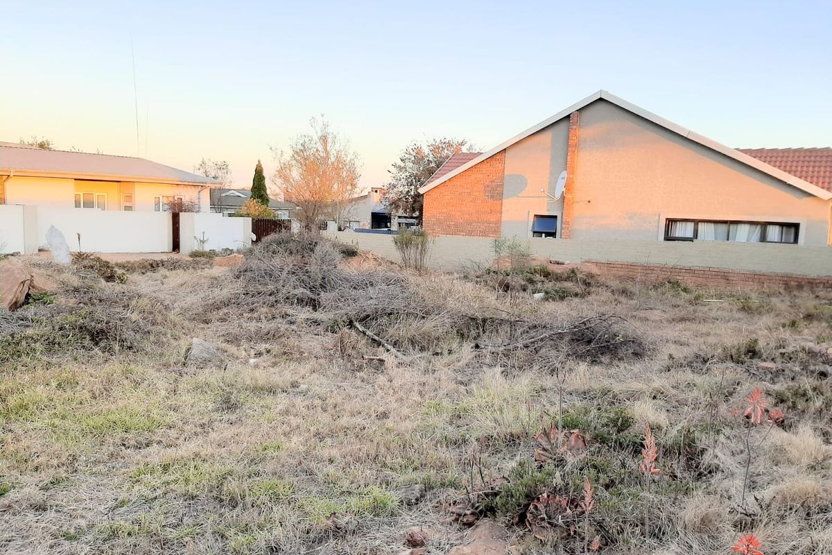 A vacant residential plot featuring dry, overgrown vegetation and perimeter boundary walls, situated in an established suburban neighborhood.