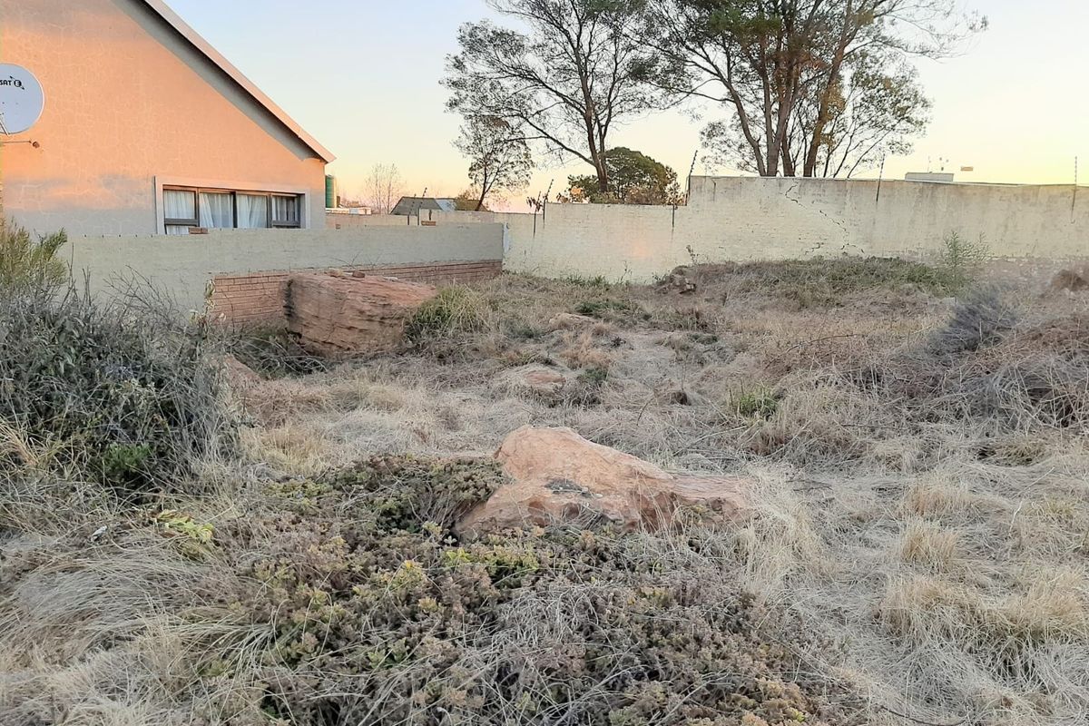 A view of a vacant residential plot featuring natural rock formations and a perimeter boundary wall, requiring clearing and landscaping.