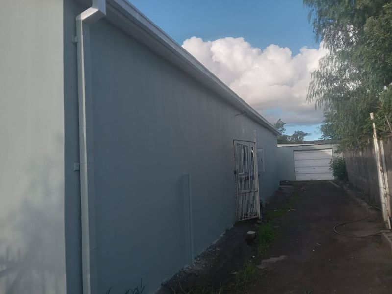 Side view of the property showing the exterior wall, guttering, security gate, and access to the rear garage.