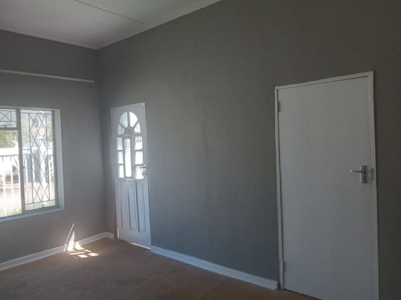 An empty living room featuring grey walls, carpet flooring, and security features on the window and door.